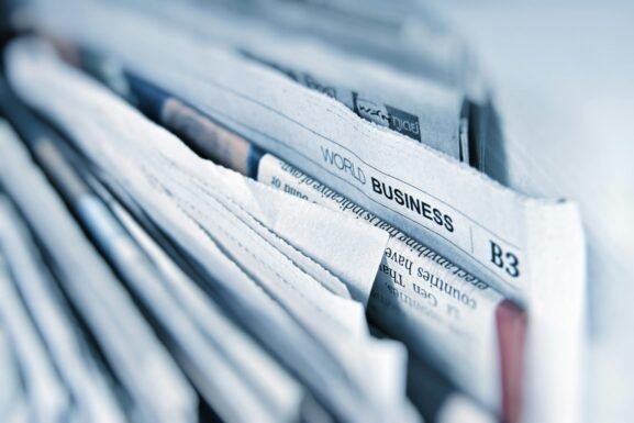 A close-up of a stack of newspapers, with the headline World Business visible, suggesting global business news—perhaps even features on innovations like golf simulators or trends in golf sim technology. The edges of the papers are slightly rumpled.