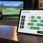 Tablet on a counter showing a golf simulator bay booking calendar, with a simulator bay in the background