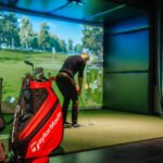 Golfer lining up a putt inside a golf simulator bay at an indoor golf venue, with a TaylorMade staff bag in the foreground